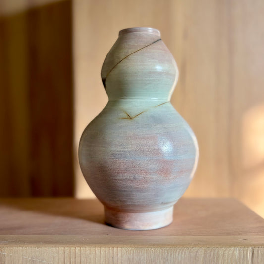 A porcelain vase that is a variation of the classic moon jar shape. The vase shape is defined by two moon jars that were wheel thrown one over another. The vase was fired in a saggar fire process, giving it its blue, green, pink and golden tones.