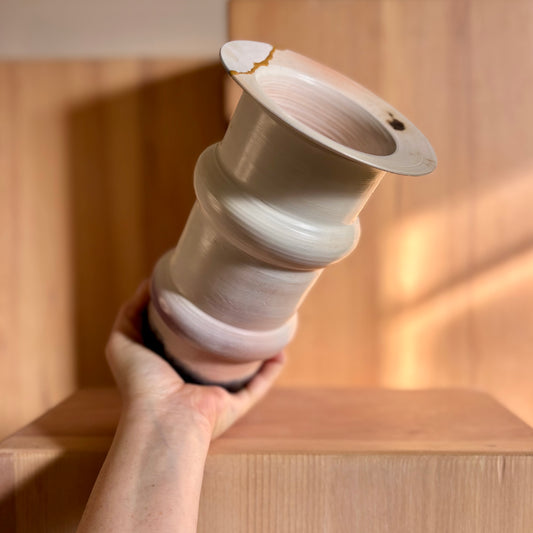 A hand holding a porcelain saggar-fired vase in peach tines and a kintsugi style rim. Made by Hillit Wahlberg