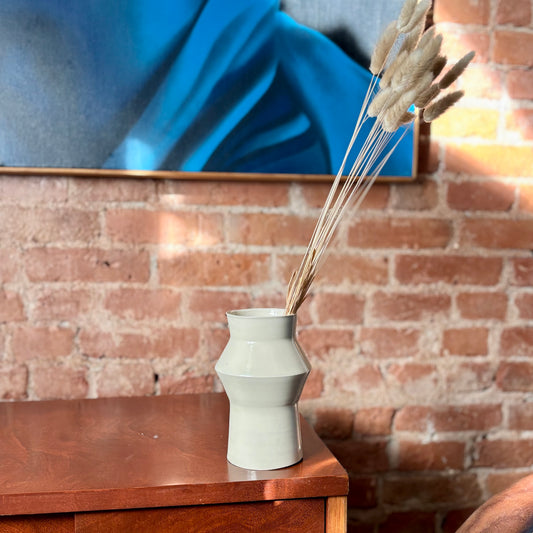 A white porcelain angular vase with dry flowers, sitting on a vintage cabinet. Made by Hillit Wahlberg