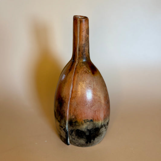A rustic ceramic vase with a bulbous body and a narrow neck, featuring a glossy finish with earthy brown, bronze, and black glaze variations, set against a plain beige background.