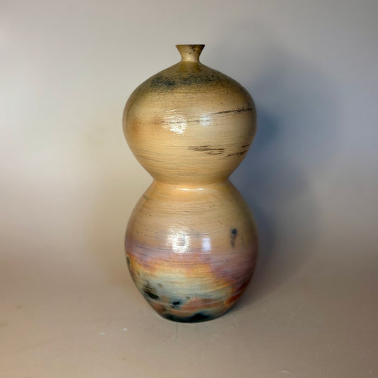 A handmade ceramic vase with a double-bulb, gourd-like silhouette, featuring a glossy finish with natural earthy color variations of beige, brown, and subtle pastel tones near the base.
