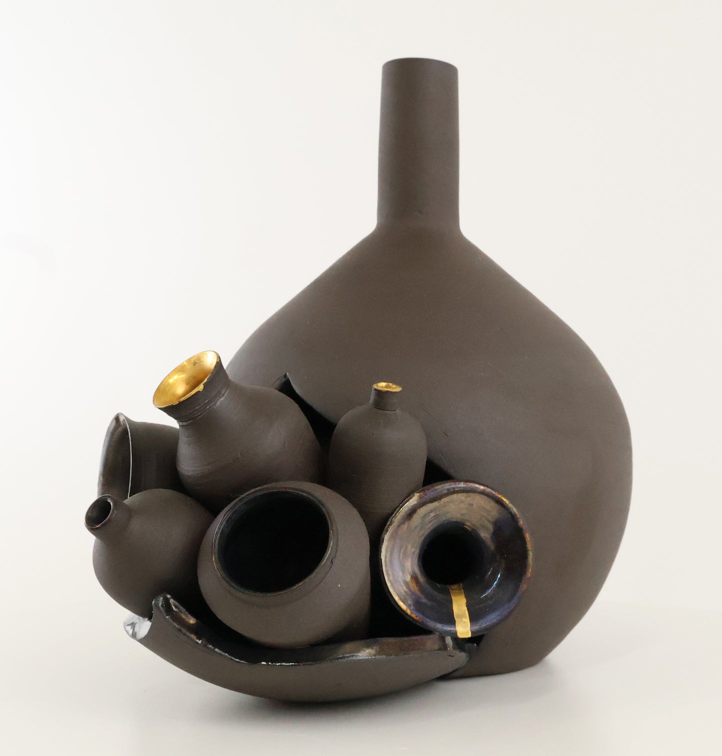 A sculptural arrangement of matte dark brown ceramic vases and vessels with small gold accents, photographed on a clean white studio background.
