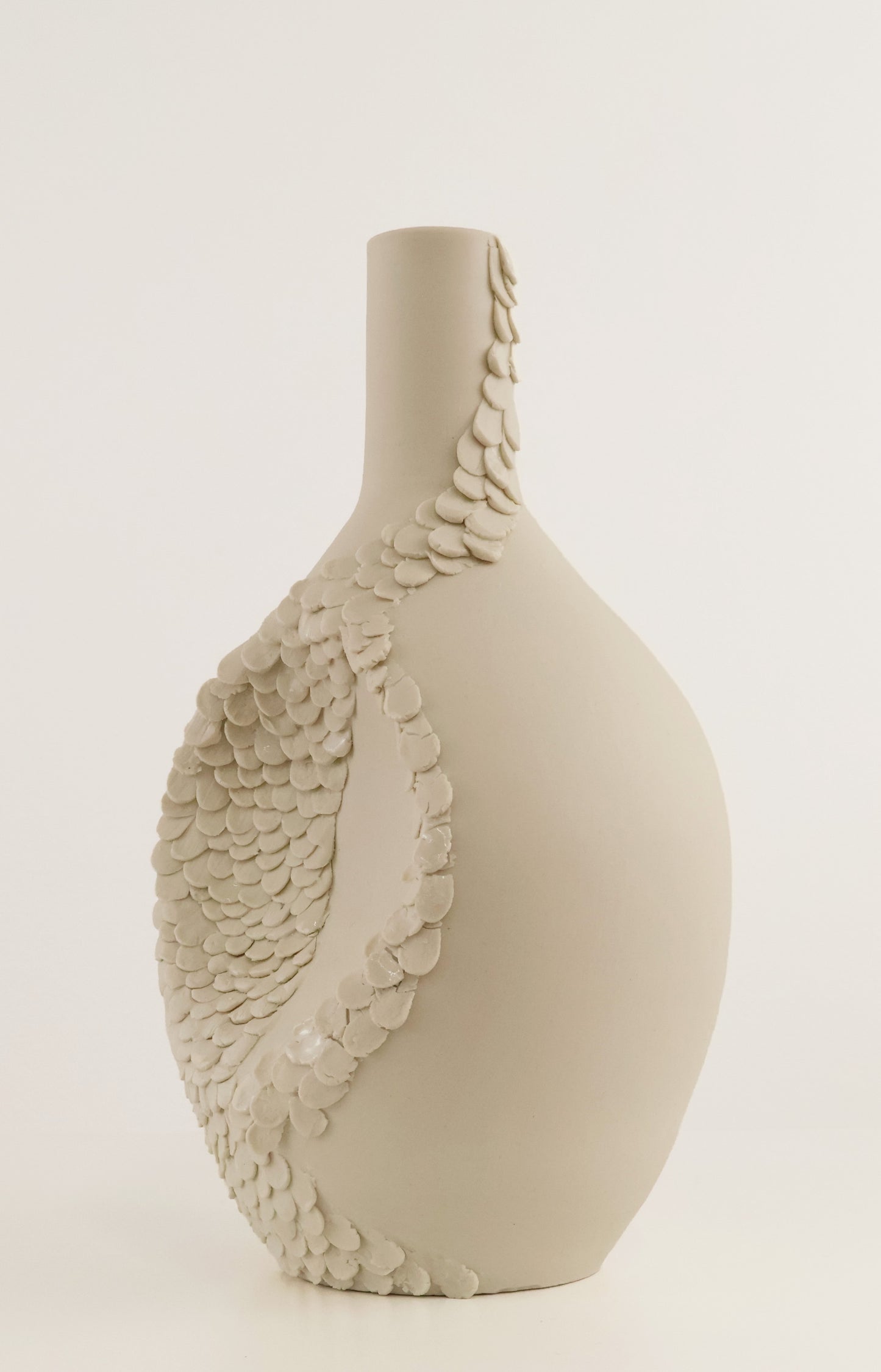 A matte ceramic vase with a bulbous body and narrow neck, decorated with a large scale-like leaf motif in a light warm gray or greige tone, shown against a plain light background.