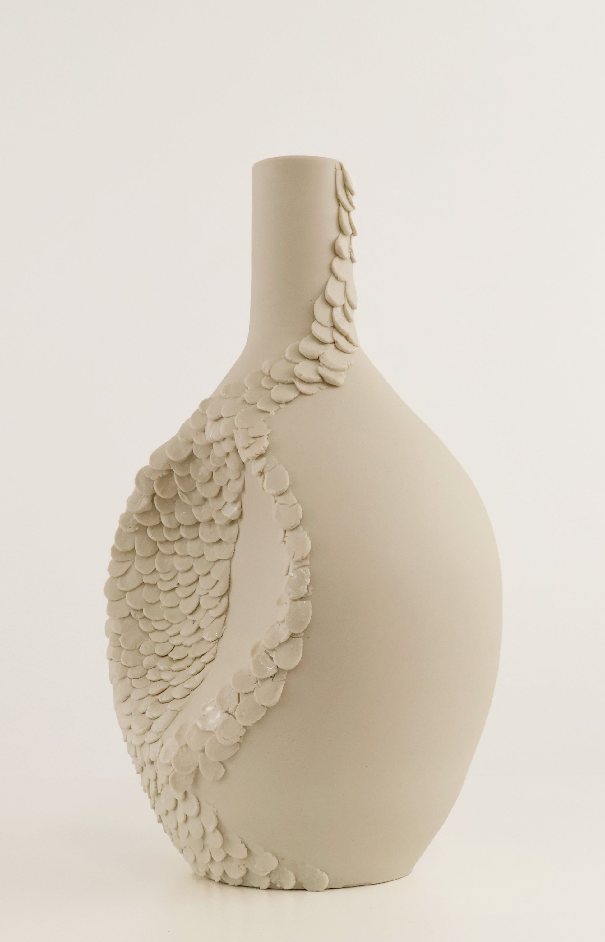 A matte ceramic vase with a bulbous body and narrow neck, decorated with a large scale-like leaf motif in a light warm gray or greige tone, shown against a plain light background.