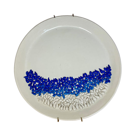 A round white ceramic plate with a decorative border of small teardrop-shaped beads in blue and white, arranged in a curved wave pattern along the lower half.