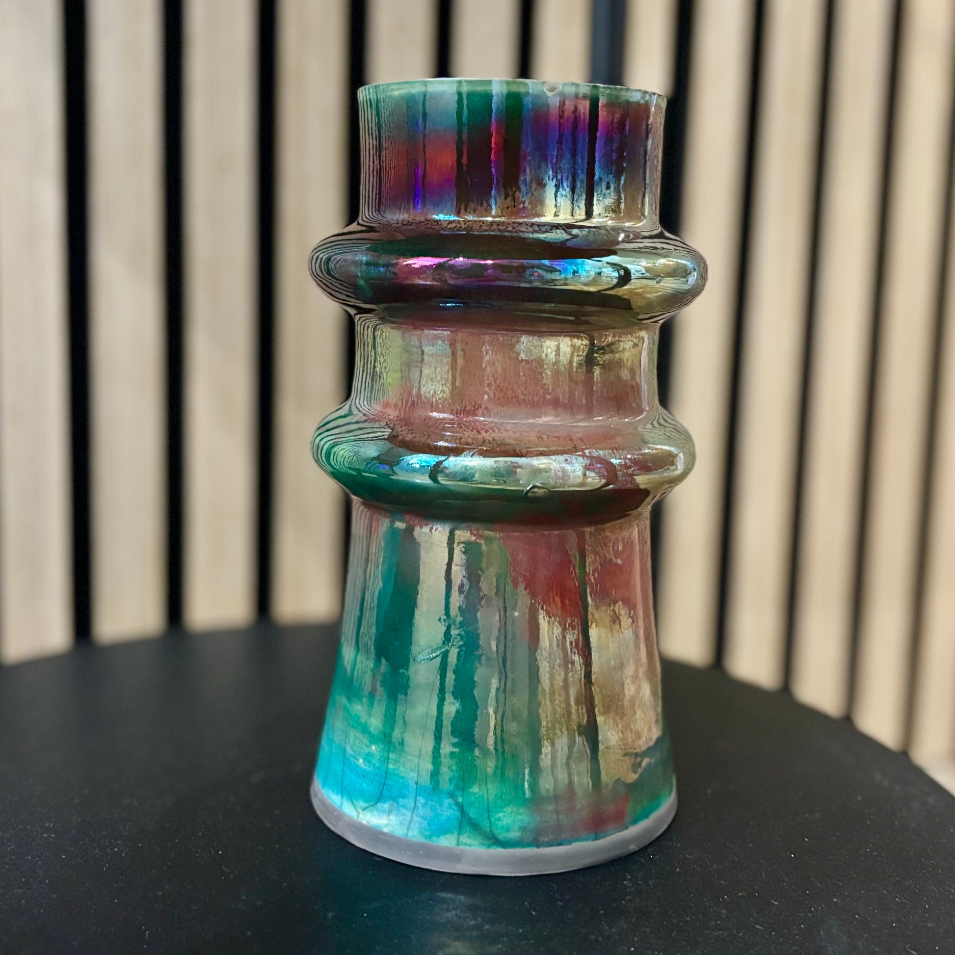 Multicolored porcelain vase on a black surface with a striped background