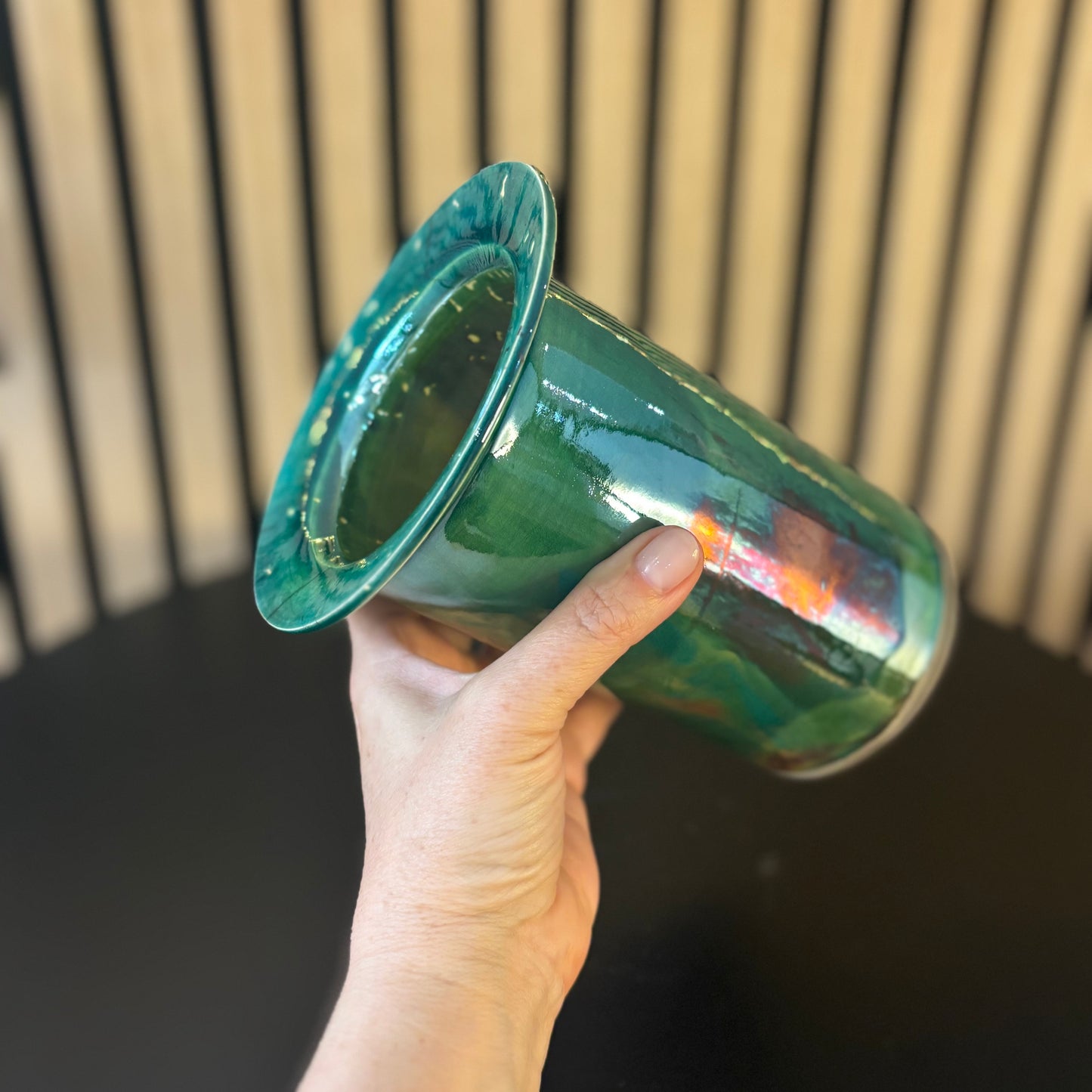 Hand holding a green ceramic pot against a neutral background