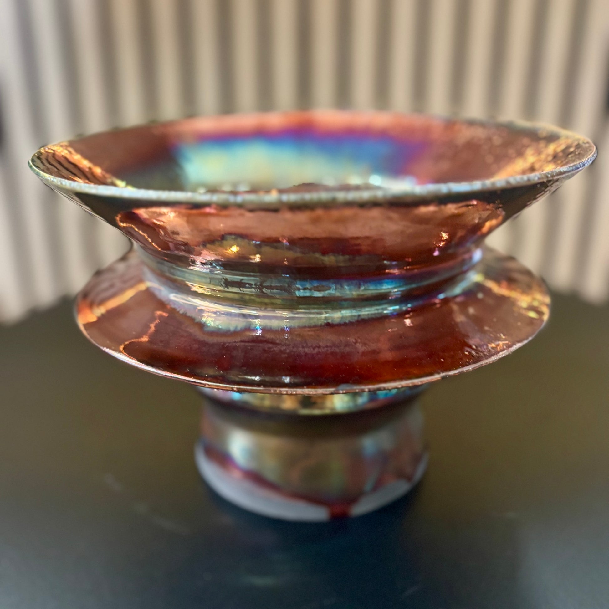 Copper-colored porcelain vessel with a ribbed texture on a reflective surface