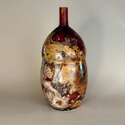 A handmade ceramic vase with a bulbous, rounded body and a short, narrow neck, featuring a marbled, organic glaze pattern in brown, gold, beige, and deep red-burgundy tones, set against a plain light gray background.