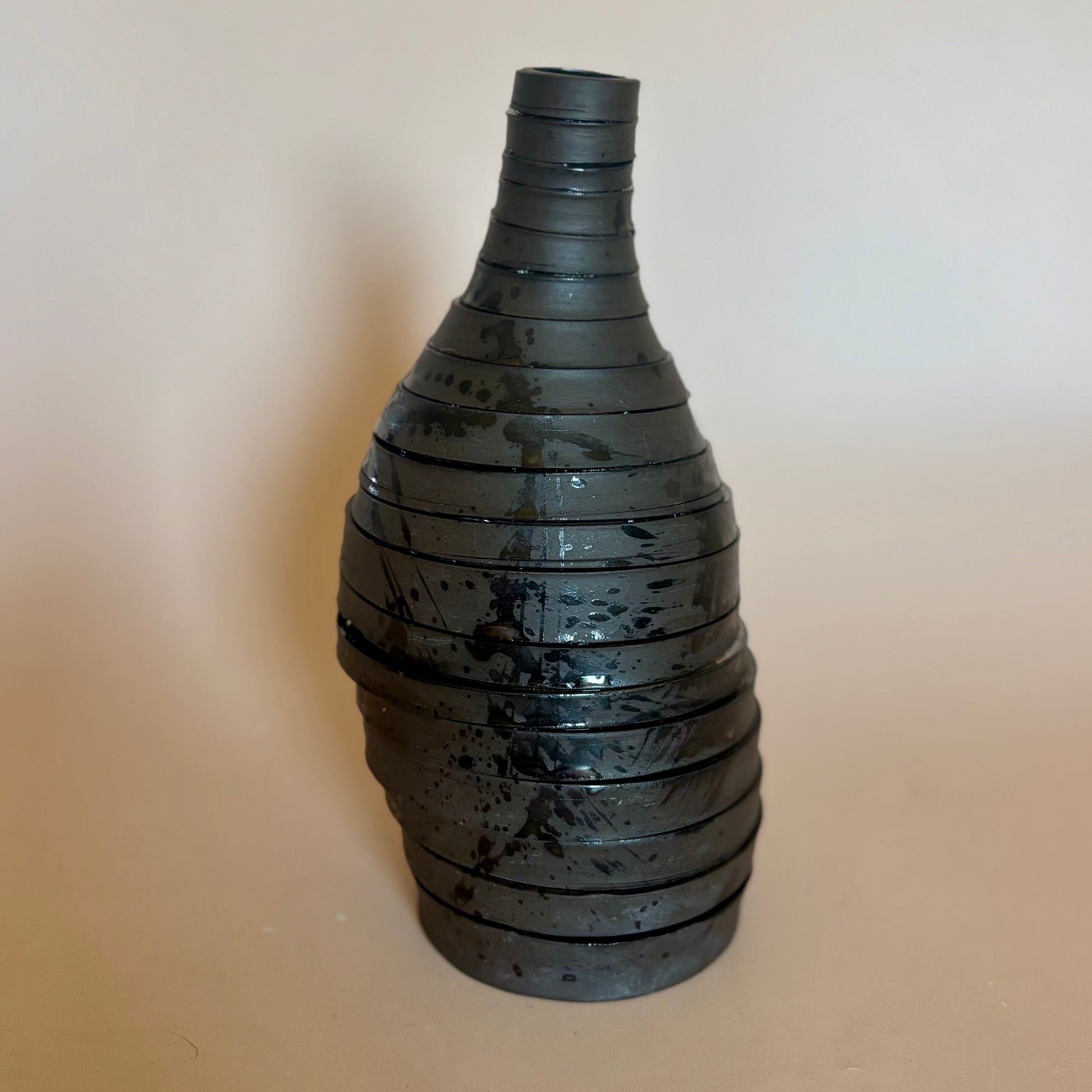 A black ceramic vase with a textured, ribbed spiral design and glossy finish, set against a plain beige background.