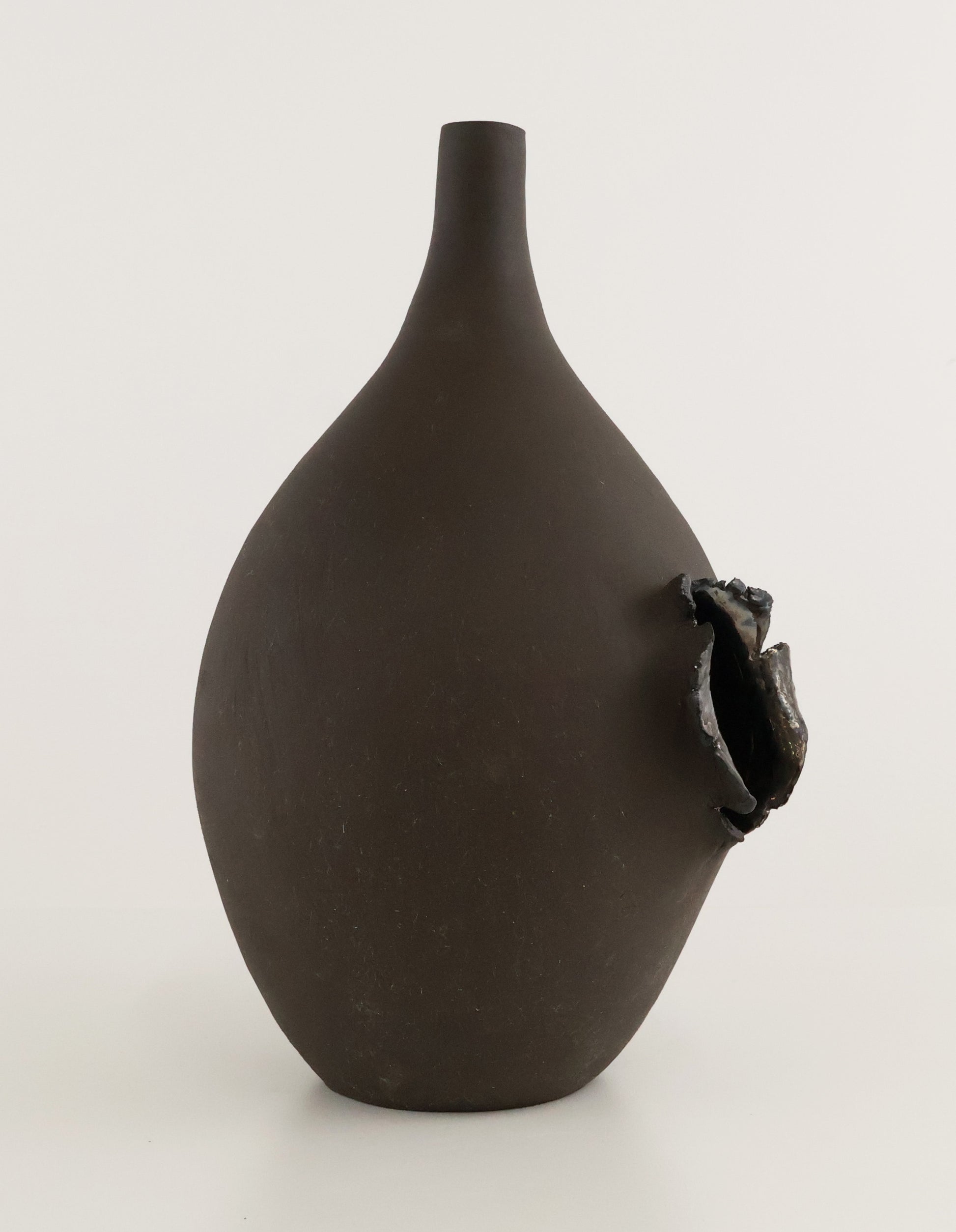 A dark brown matte ceramic vase with a narrow neck and a textured, organic protruding opening on the side, set against a plain light gray background.